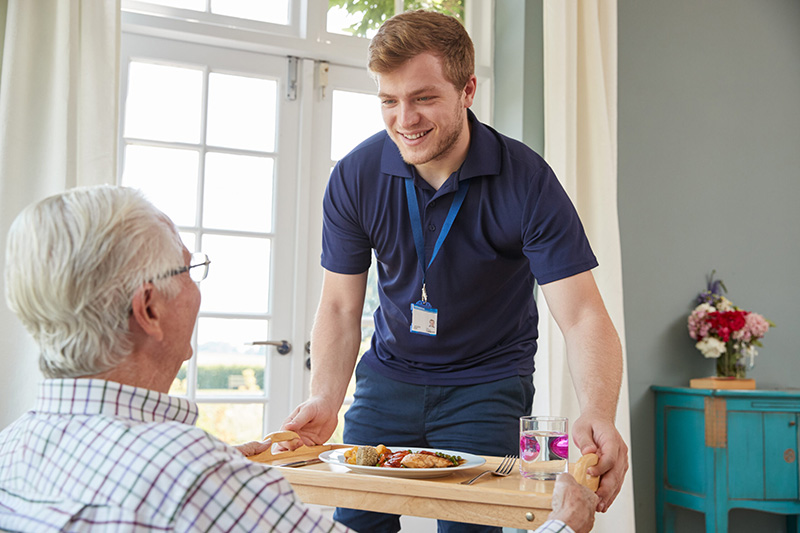 A young, smiling man serving a meal to an older person